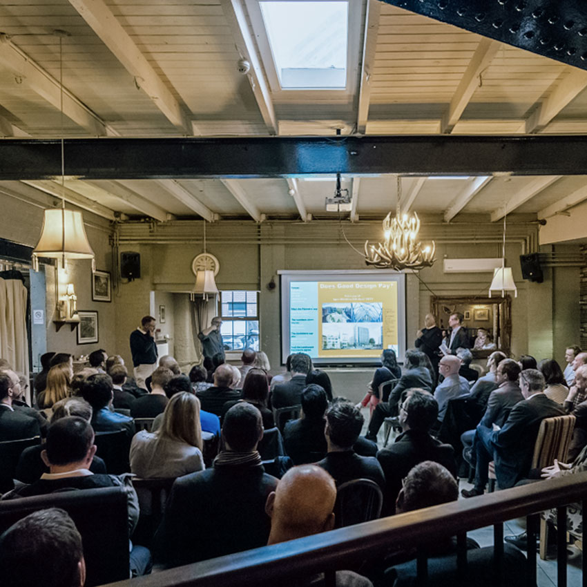 Large full width photo of people sitting in a conference centre looking right towards the front where the speaker is