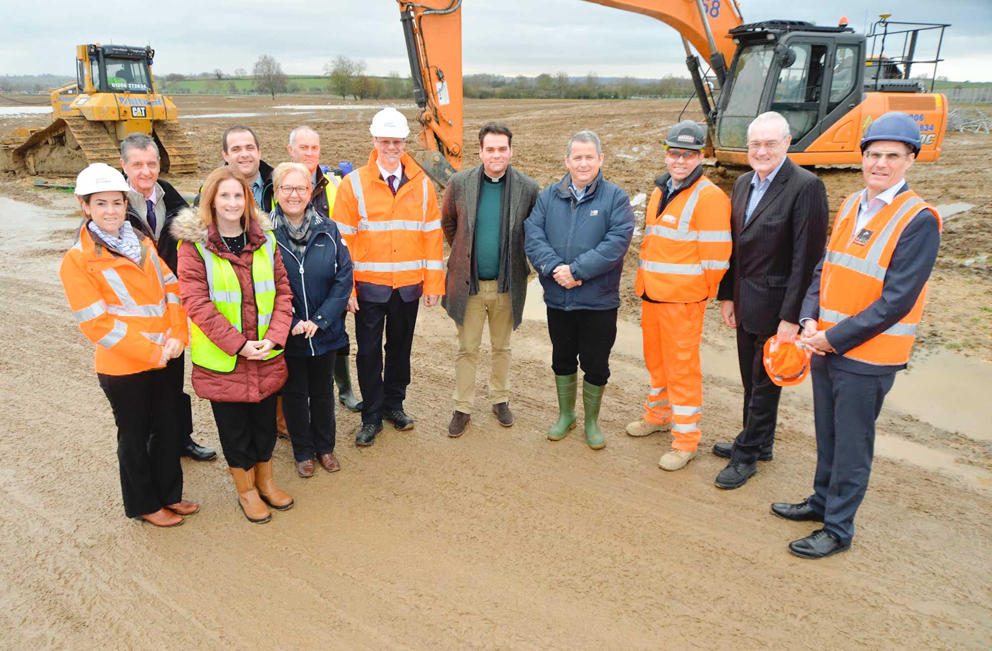 On-site photo of the team in hard hats and high visibility jackets with diggers in the background