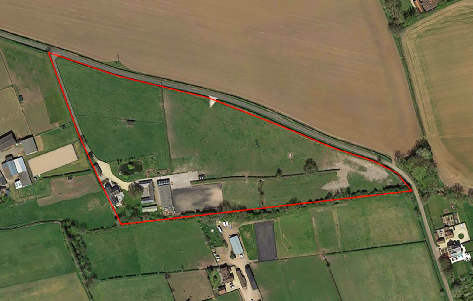 Aerial photographic view of the site area, shows many green fields, then a horizontal triangle with a red outline in the middle marking the area