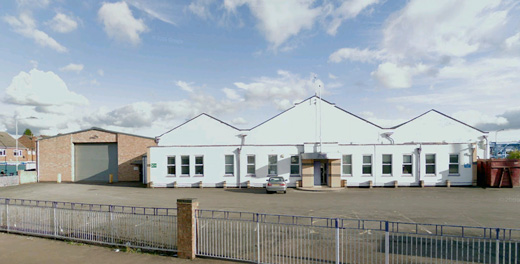 Photo of the front of the site before remodeling. Shows single storey triangular factory type buildings